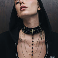Woman wearing a black beaded choker and layered necklaces against a dark background