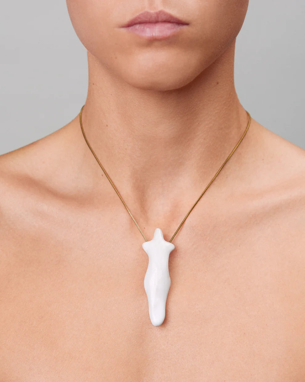 Person wearing a necklace with a white pendant on a neutral background